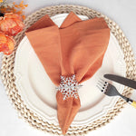 Une élégante table de fête avec une nappe tressée, des serviettes en tissu orange et une décoration hivernale.