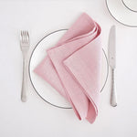 Un service de table élégant avec une serviette rose pâle, une fourchette et un couteau sur un plateau blanc.