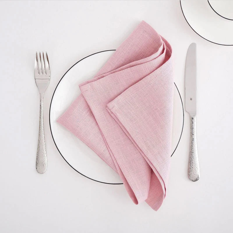 Un service de table élégant avec une serviette rose pâle, une fourchette et un couteau sur un plateau blanc.