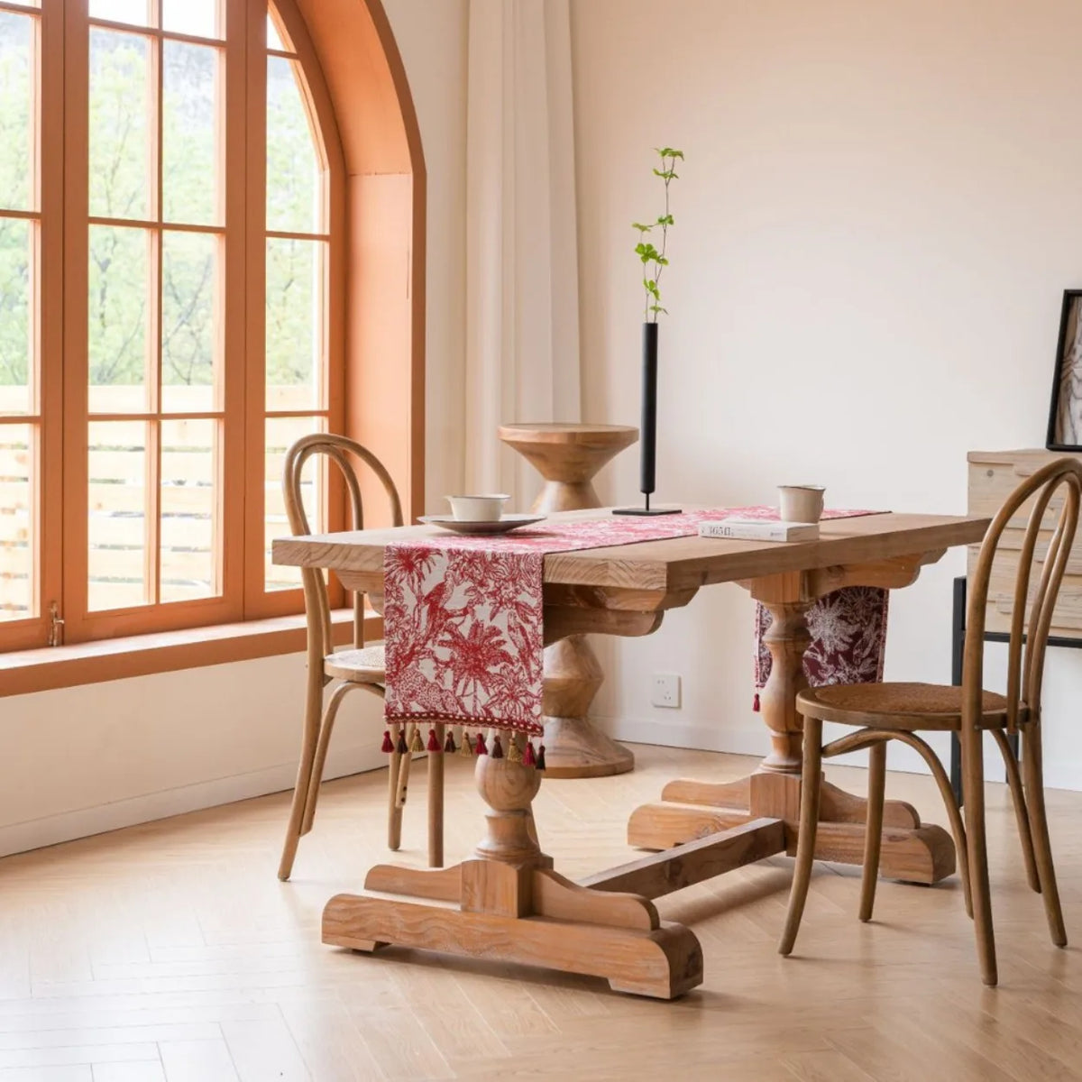 Cette image montre une salle à manger lumineuse avec de grandes fenêtres, une table en bois massif et des chaises rustiques, décorée avec des accessoires colorés.
