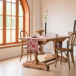Cette image montre une salle à manger lumineuse avec de grandes fenêtres, une table en bois massif et des chaises rustiques, décorée avec des accessoires colorés.
