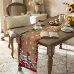Une table de salle à manger joliment décorée dans un style rustique pour les fêtes de Noël, avec un chemin de table en tissu imprimé de motifs de Noël et de camions rouges vintage, un livre ouvert posé dessus, et des éléments de décoration comme des fleurs et des fruits.