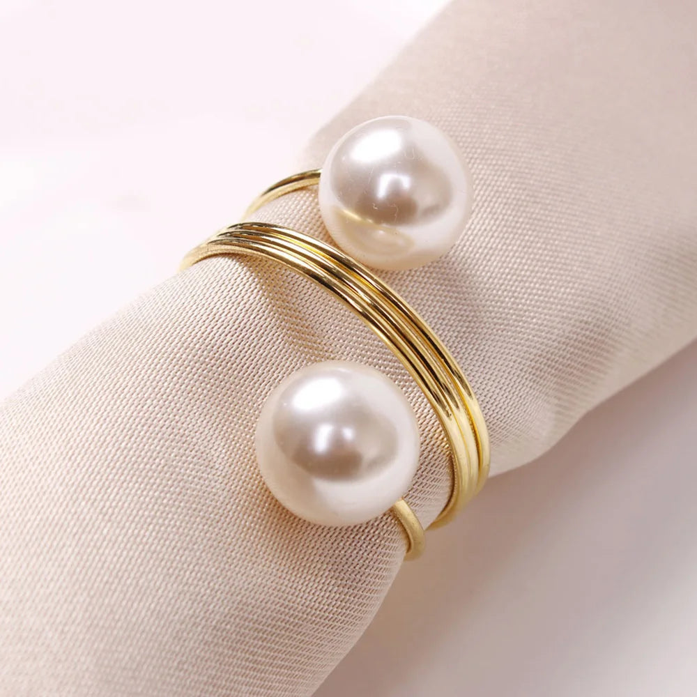 Une élégante bague en or sertie de deux perles blanches posée sur un tissu beige.