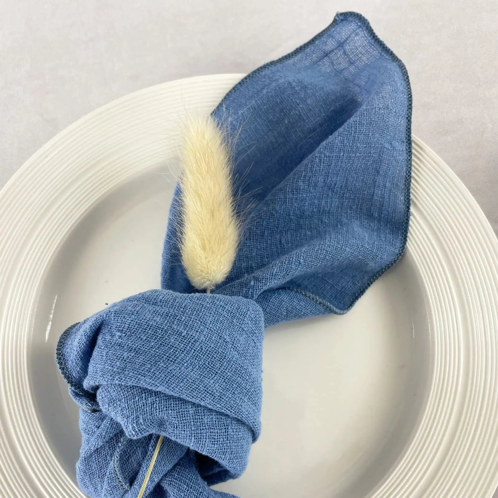 Une serviette en lin bleu avec une décoration en plume posée sur une assiette blanche.