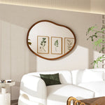 Salon élégant avec miroir mural ovale en bois, cadres décoratifs de feuillage et canapé blanc confortable.