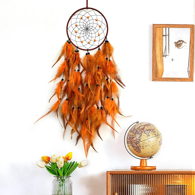 Attrape-rêves décoratif aux plumes oranges suspendues à un cadre en métal enroulé, entouré de tulipes dans un vase et d'un globe terrestre sur un meuble en bois.