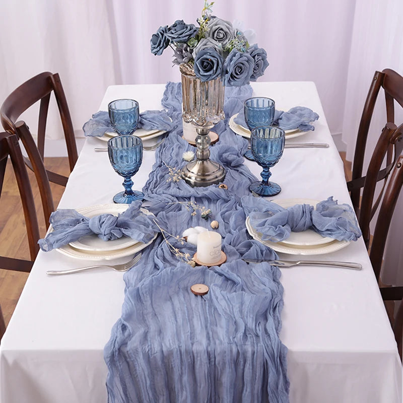 Un décor de table élégant avec un bouquet de roses bleu pâle, des verres à pied bleu marine et un chemin de table en tissu gris.