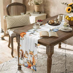 Cette table de petit-déjeuner chaleureuse et rustique met en scène une décoration automnale avec des fleurs, des fruits et un livre ouvert, créant une ambiance accueillante et cosy.