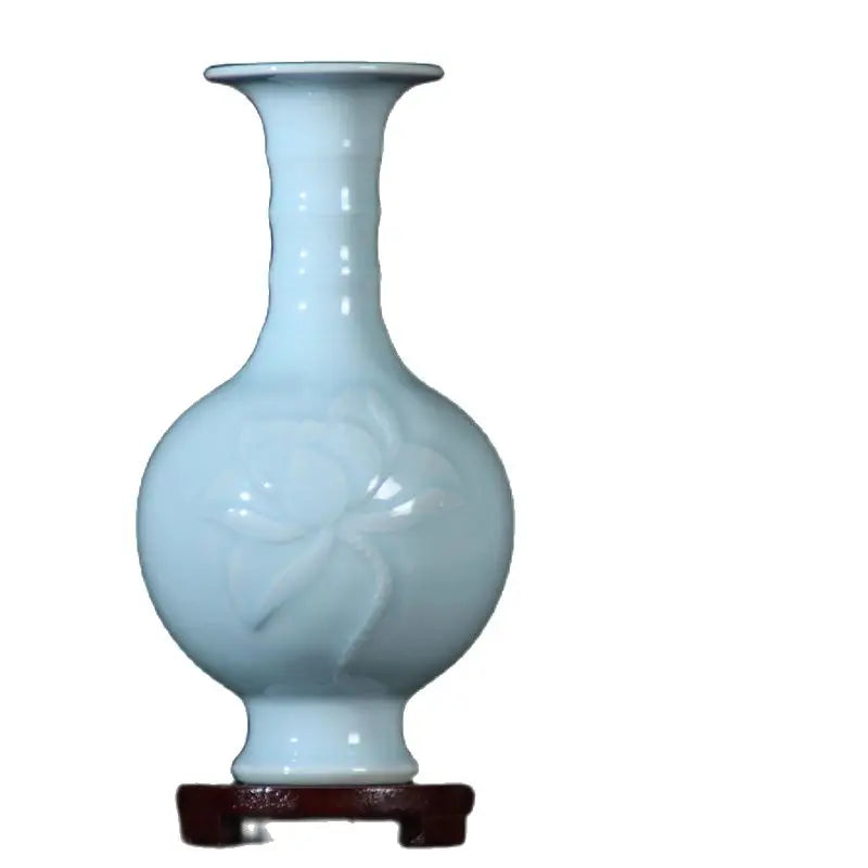 Un vase en porcelaine bleu pastel avec un motif de fleur incrusté, reposant sur un support en bois.