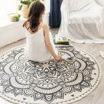 Une femme de dos assise sur un tapis rond avec un motif mandala noir et blanc dans une chambre lumineuse.