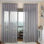 Rideaux élégants de couleur gris clair dans un salon contemporain, apportant une touche de sophistication et de modernité à la décoration intérieure. L'installation permet une diffusion idéale de la lumière naturelle tout en assurant une certaine intimité. Accessoires adjacents en harmonie avec le style lumineux et épuré.