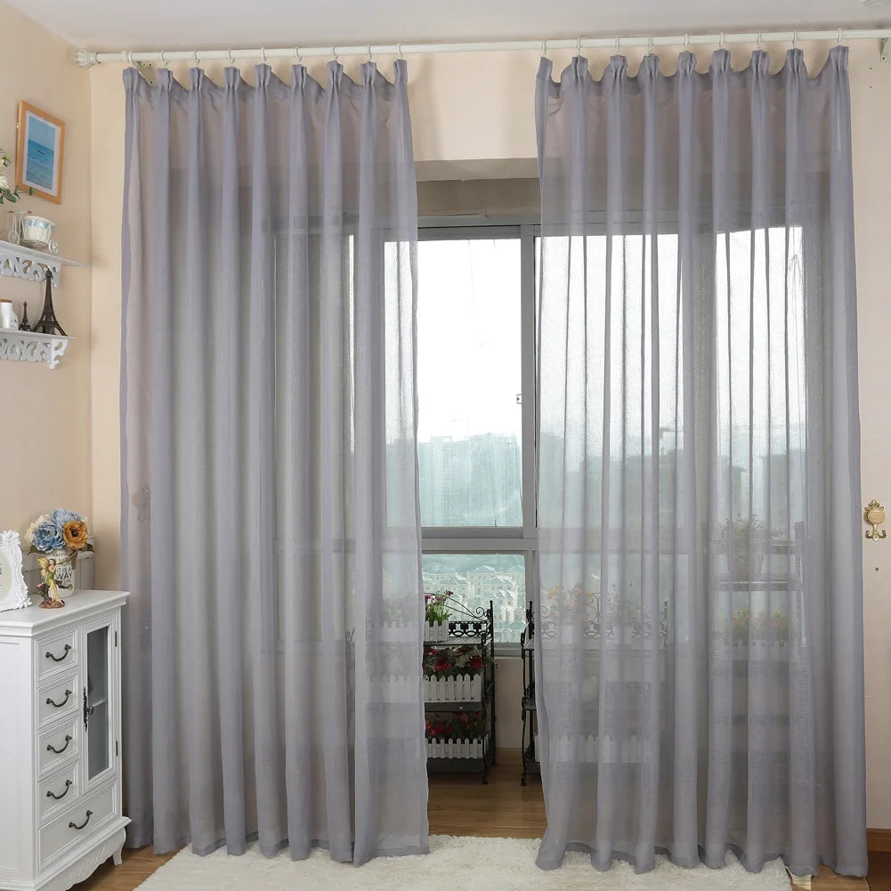 Rideaux transparents gris élégants pour un salon lumineux, suspendus sur une tringle blanche, devant une grande fenêtre. Parfait pour filtrer la lumière tout en maintenant une atmosphère moderne et épurée. Décor idéal pour ajouter une touche de sophistication à n'importe quelle pièce.
