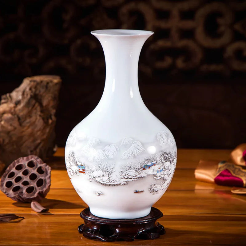 Un vase blanc décoré d'un paysage d'hiver avec des montages enneigés sur un socle en bois sombre.