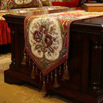 Un chemin de table orné de motifs floraux colorés, agrémenté de pompons et de franges, décorant élégamment un meuble en bois sombre.