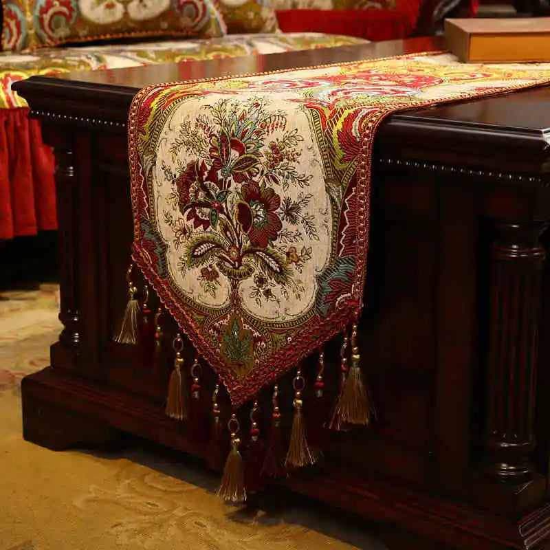 Cette élégante nappe décorative sur un coffre en bois sombre met en valeur un motif floral brodé de couleurs chaudes, créant une ambiance chaleureuse et raffinée.
