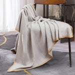 Une élégante couverture grise et blanche ornée de motifs géométriques, posée sur une chaise en bois.