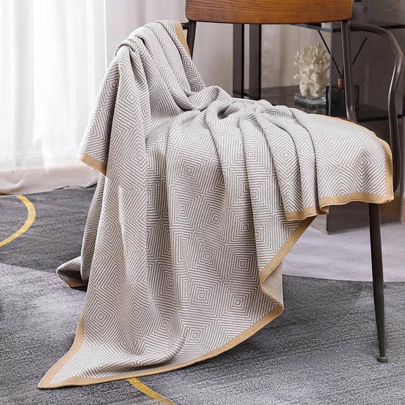 Une élégante couverture grise et blanche ornée de motifs géométriques, posée sur une chaise en bois.