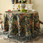 Une belle table décorée avec un magnifique nappage fleuri, une bouteille de vin, des verres, des raisins et un bouquet de fleurs, créant une ambiance chaleureuse et accueillante.