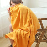 Une femme vêtue d'une couverture moelleuse et jaune se repose sur une chaise en bois.