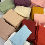 Une collection de piles de tissus en couleurs vives et douces, y compris des tons de vert, de rose, de rouge et de jaune, créant une présentation élégante et harmonieuse.