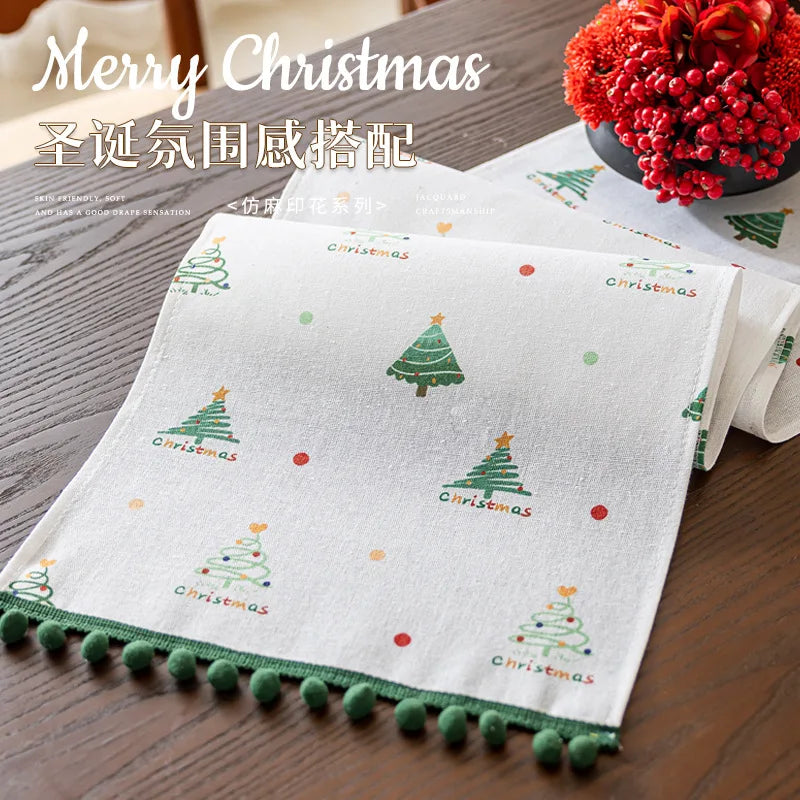 Joli chemin de table de Noël avec des imprimés d'arbres de Noël colorés et une bordure avec des pompons verts, créant une atmosphère festive et chaleureuse pour les célébrations de Noël.