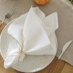 Cette image montre une assiette blanche avec de belles serviettes de table pliées en forme de fleur, sur une table en bois avec une citrouille orange.