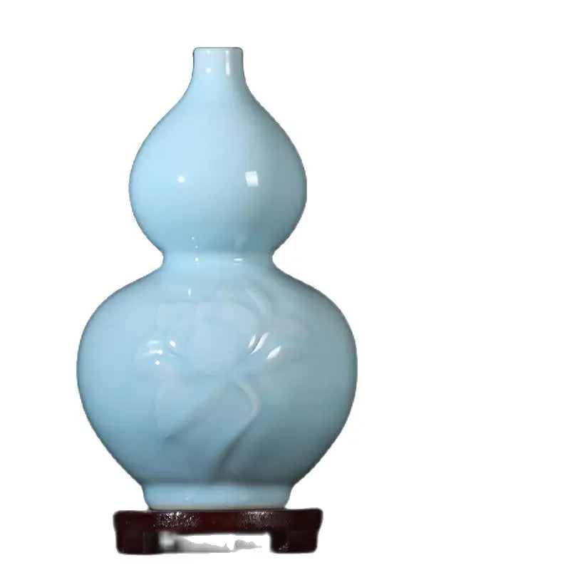 Vase de forme gourde en verre opaque de couleur bleue pastel posé sur un support en bois foncé.