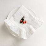 Une grappe de petites baies rouges posée délicatement sur un linge blanc plié, offrant une composition minimaliste et élégante.