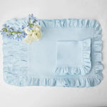 Coque de lit en satin bleu clair avec une bordure plissée et une fleur blanche posée sur le côté.