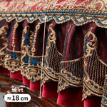 Une jupe ornée de magnifiques motifs floraux et de broderies dorées sur un fond rouge foncé, avec des détails bleus qui ajoutent de la profondeur et de la richesse à ce vêtement traditionnel.