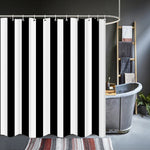 Rideau de douche à rayures noires et blanches suspendu sur une tringle arrondie, installé devant une baignoire en métal style industriel. Salle de bain élégante avec échelle porte-serviettes et tapis décoratif
