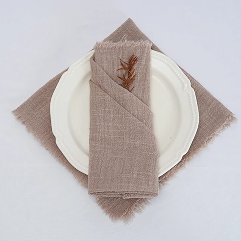 Une serviette de table beige enroulée sur une assiette blanche, ornée d'une petite branche de bois.