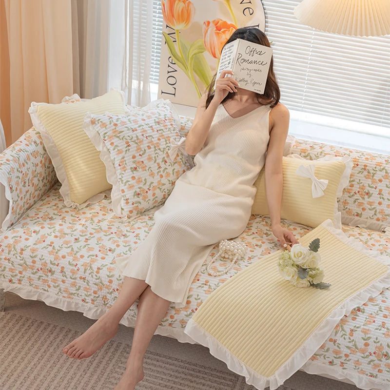 Une jeune femme vêtue d'une robe blanche confortable se détend sur un lit décoré de motifs floraux et de coussins jaunes.