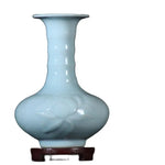 Vase en céramique bleu pâle aux formes élégantes et épurées, posé sur un support en bois foncé.