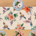 Une scène naturelle et colorée, avec des fleurs tropicales, des colibris volants et des roses roses sur un fond de bois clair.
