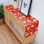 Meuble en bois avec un chemin de table décoré de motifs festifs rouges et dorés.