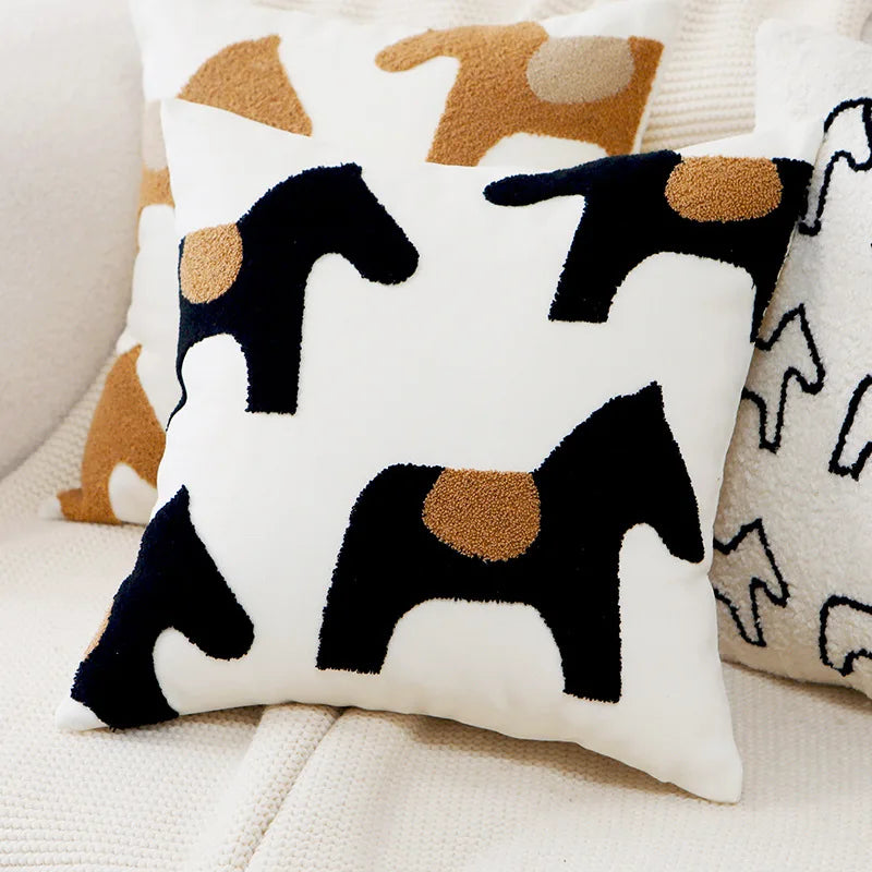 Coussin décoratif avec des motifs de chevaux stylisés en noir et marron sur un fond blanc.