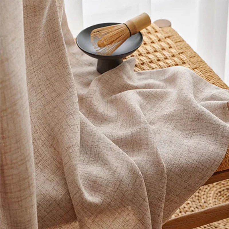 Gros plan sur un rideau écru à motif croisé, posé sur une chaise tressée avec un fouet à thé matcha en décoration.