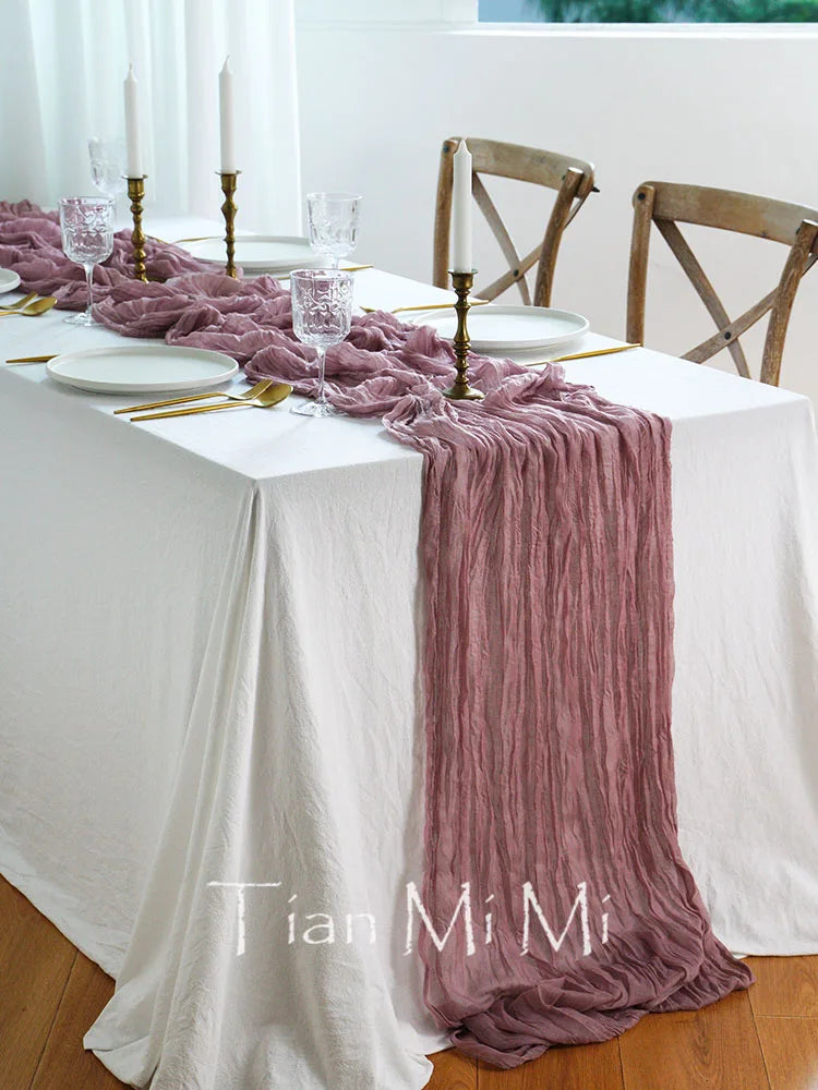 Une magnifique table dressée pour un repas spécial, avec des assiettes blanches, des verres de cristal, des chandelles et une élégante nappe rose pâle qui ajoute une touche de sophistication à l'ensemble.