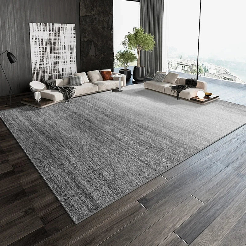 Pièce spacieuse et moderne avec un grand canapé et un tapis gris texturé, donnant sur une fenêtre avec vue sur l'extérieur.