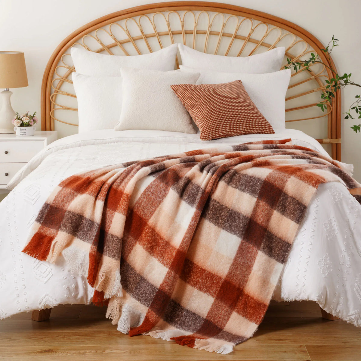 Un lit double au style rustique avec une tête de lit en rotin, une couverture à carreaux dans des tons chauds et des oreillers assortis pour une atmosphère cocooning.