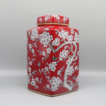 Un élégant pot de stockage en céramique de couleur rouge vif, décoré de magnifiques fleurs de prunier blanc et de papillons, évoquant une ambiance orientale chaleureuse et raffinée.