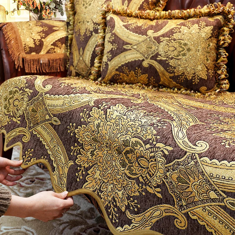 Coussins décoratifs brodés de motifs floraux et de motifs abstraits dans des tons dorés et bruns, disposés sur un canapé ou une chaise.