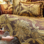 Coussins décoratifs brodés de motifs floraux et de motifs abstraits dans des tons dorés et bruns, disposés sur un canapé ou une chaise.