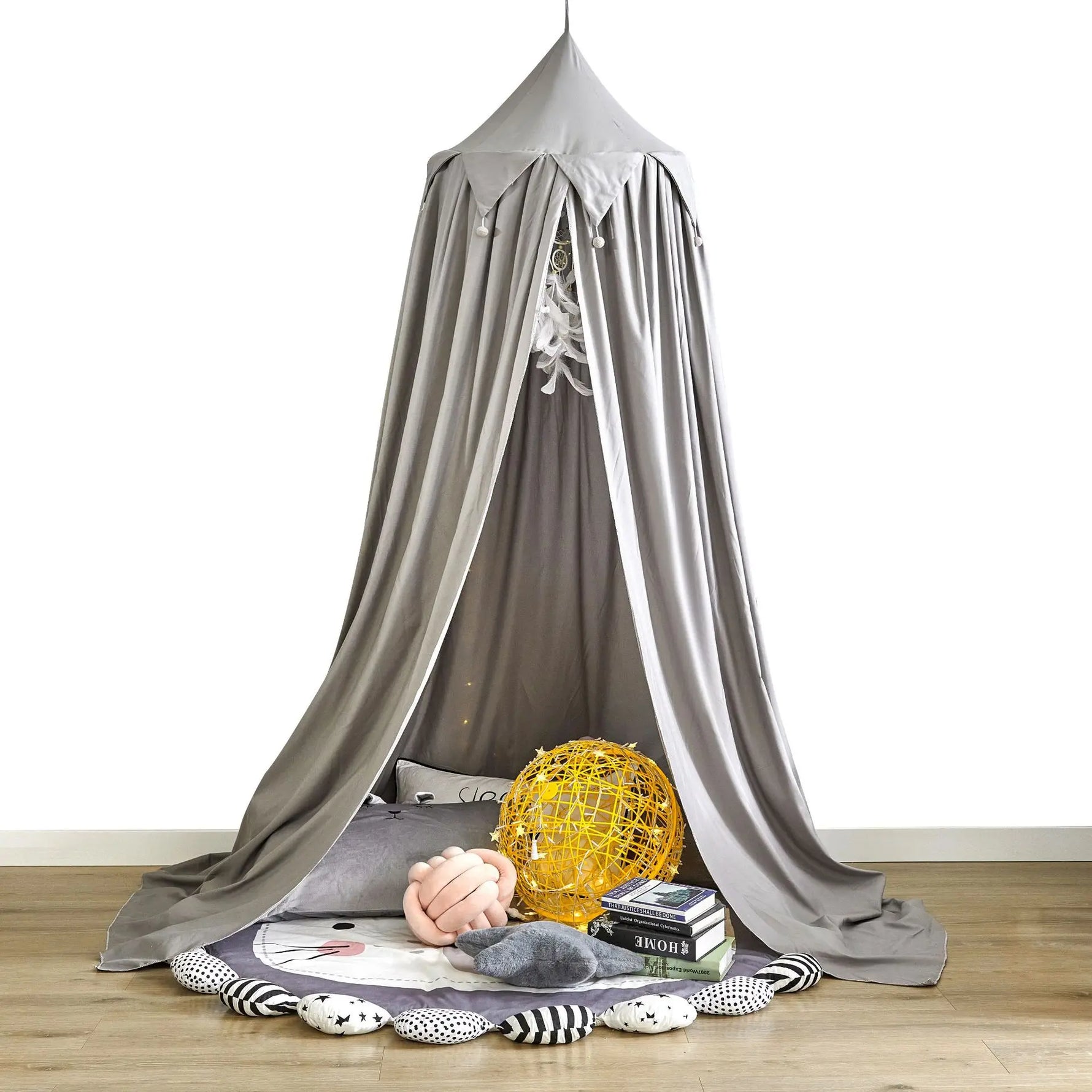Un coin cocooning douillet et confortable, avec un dôme gris suspendu, des coussins moelleux, un gros ballon jaune et des livres, créant un espace intime et relaxant.