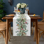 Sur une table élégante ornée de verres à vin et de fleurs blanches, un chemin de table décoré de motifs floraux et d'oiseaux crée une ambiance chaleureuse et festive.