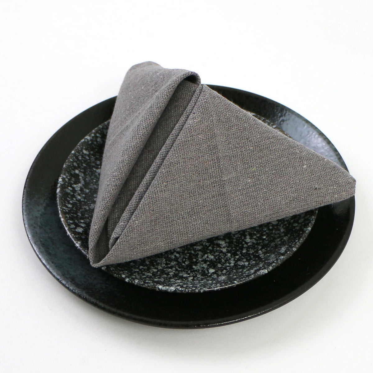 Un élégant pliage de serviette gris en textile, décoré avec soin sur un plat de service en céramique noire.