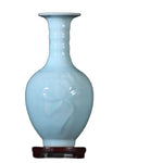 Élégant vase en céramique d'un bleu clair, avec un motif ornemental subtil, sur un socle en bois.