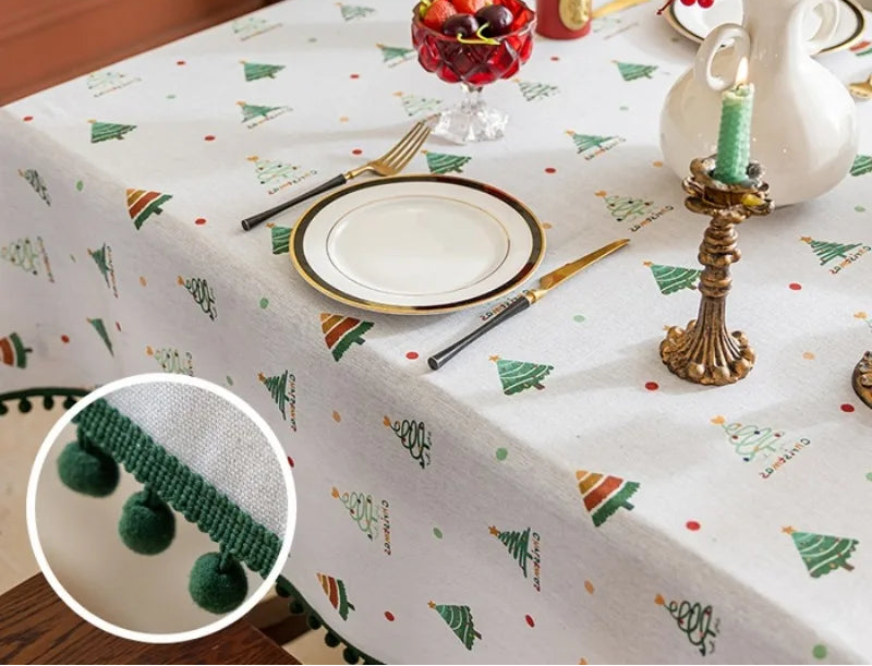 Nappe de Noël blanche avec motif d'arbres de Noël verts et rouges, assiette et ustensiles sur la table, bougeoir décoratif et décorations de baies rouges.