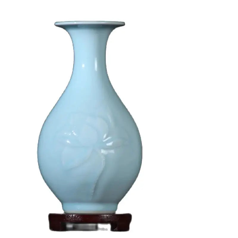 Vase en porcelaine bleu pâle avec forme élancée et élégante, posé sur un présentoir en bois foncé.